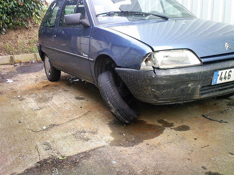 Au garage, la voiture de trois quarts avant sur un sol en béton mouillé : aile et pare-chocs avant enfoncés.